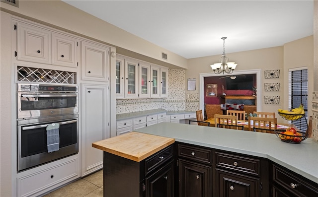 kitchen with light tile patterned flooring, white cabinetry, a chandelier, stainless steel double oven, and backsplash