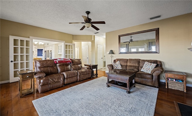 living room featuring dark wood-type flooring, ceiling fan with notable chandelier, and a textured ceiling