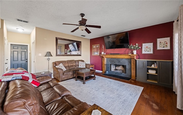 living room featuring ceiling fan, a high end fireplace, dark hardwood / wood-style floors, and a textured ceiling