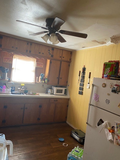 kitchen with ceiling fan, white appliances, dark hardwood / wood-style floors, and wooden walls