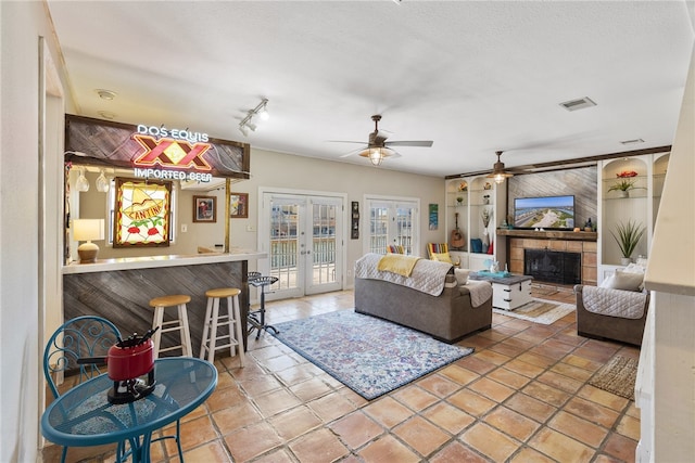 tiled living room with indoor bar, ceiling fan, french doors, a fireplace, and built in shelves