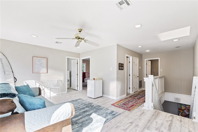 living room featuring ceiling fan, light hardwood / wood-style floors, and a skylight