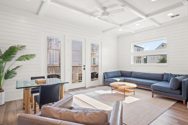 living room with coffered ceiling, wooden walls, hardwood / wood-style flooring, ceiling fan, and beamed ceiling