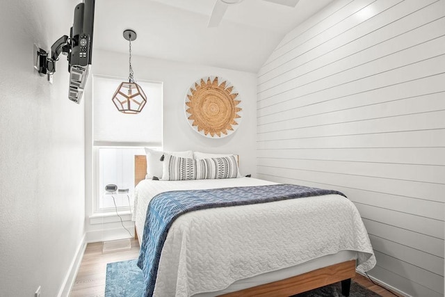 bedroom featuring hardwood / wood-style flooring, ceiling fan, wooden walls, and vaulted ceiling