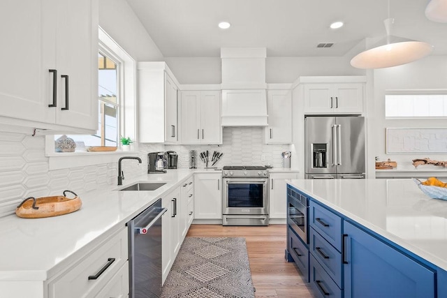 kitchen with appliances with stainless steel finishes, tasteful backsplash, blue cabinets, decorative light fixtures, and white cabinets