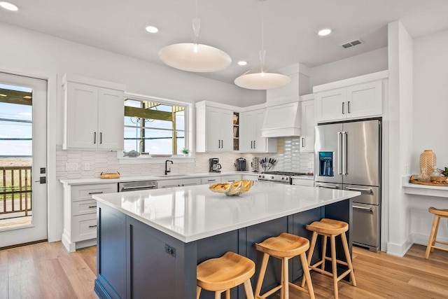 kitchen featuring appliances with stainless steel finishes, custom range hood, sink, white cabinets, and a kitchen island