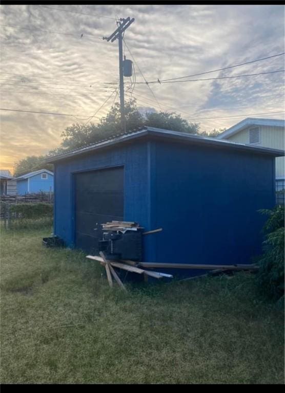 property exterior at dusk with a garage, an outbuilding, and a yard