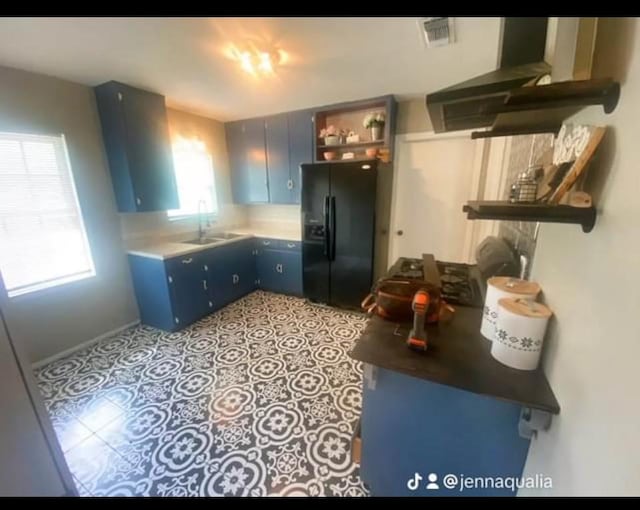 kitchen with blue cabinets, light tile patterned flooring, sink, and black fridge with ice dispenser