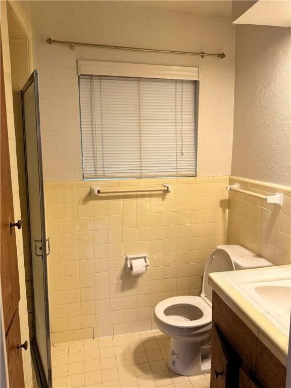 bathroom featuring toilet, tile walls, vanity, a shower with door, and tile patterned flooring