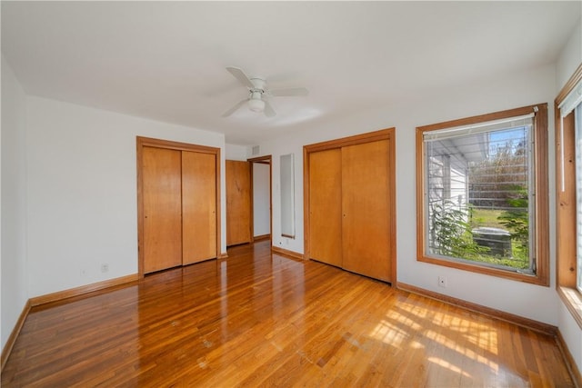 unfurnished bedroom featuring visible vents, baseboards, a ceiling fan, light wood-style floors, and multiple closets