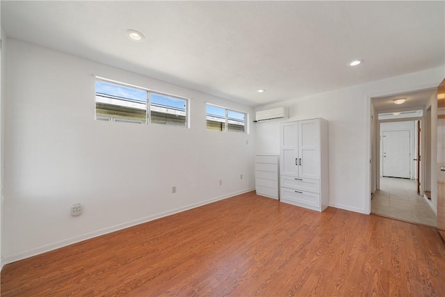 unfurnished bedroom featuring baseboards, recessed lighting, a wall mounted air conditioner, and light wood-style floors