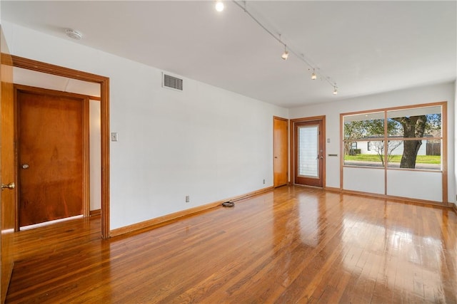 unfurnished room with hardwood / wood-style flooring, baseboards, visible vents, and rail lighting