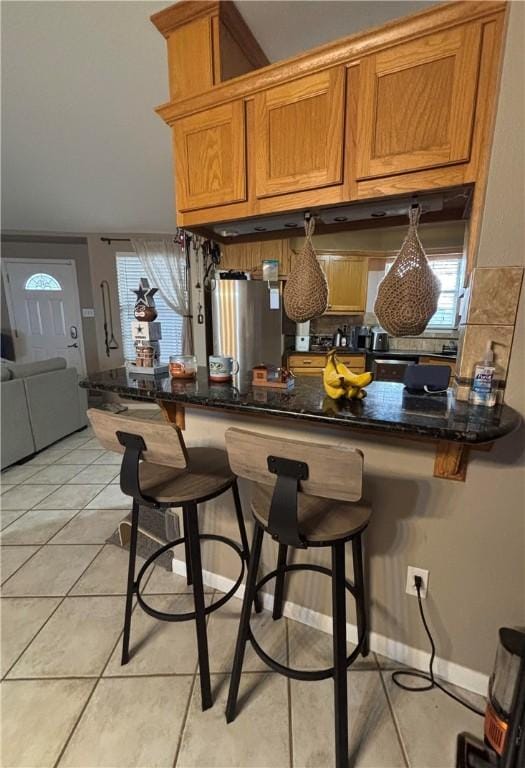 kitchen with dark stone counters, a breakfast bar, and kitchen peninsula