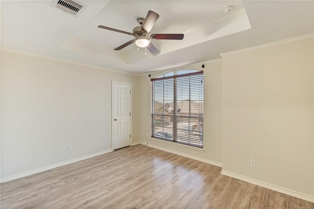 spare room featuring light wood-style flooring, visible vents, a raised ceiling, and baseboards