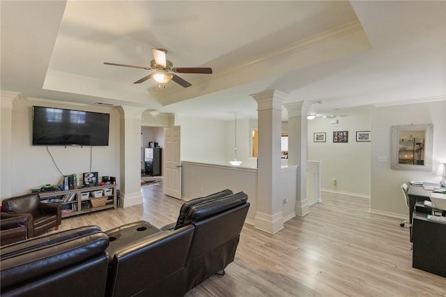 living area featuring decorative columns, a ceiling fan, ornamental molding, a tray ceiling, and light wood-style floors