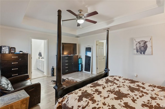 bedroom featuring a ceiling fan, ornamental molding, light wood-type flooring, a tray ceiling, and ensuite bath