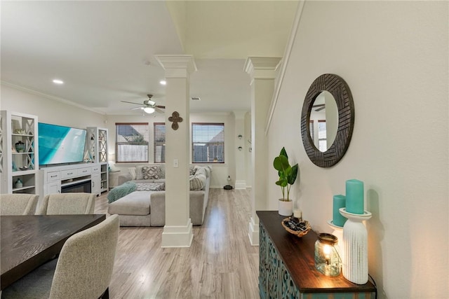 living area featuring light wood finished floors, decorative columns, a ceiling fan, ornamental molding, and a fireplace