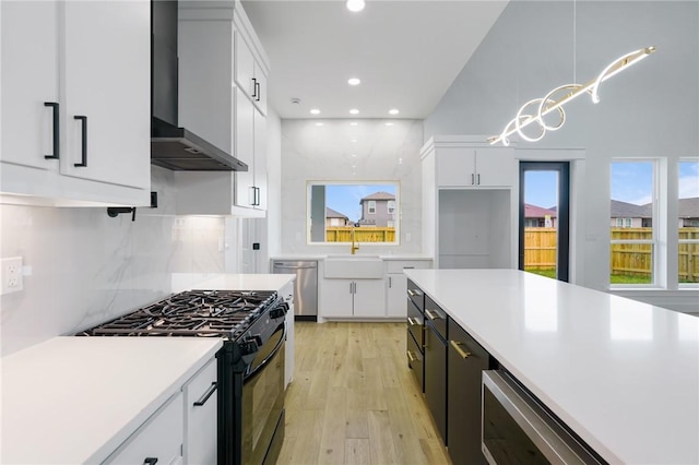 kitchen with decorative light fixtures, white cabinets, wall chimney range hood, and gas stove