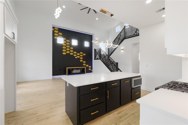 kitchen featuring a center island, pendant lighting, a high ceiling, white cabinetry, and light wood-type flooring