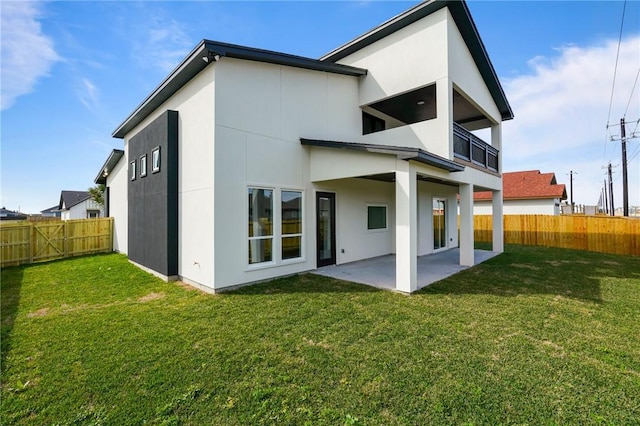 rear view of house with a balcony, a lawn, and a patio