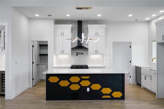 kitchen with white cabinetry, wall chimney exhaust hood, a kitchen island, and decorative light fixtures