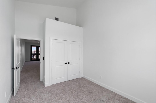 unfurnished bedroom with light carpet, a closet, and a towering ceiling