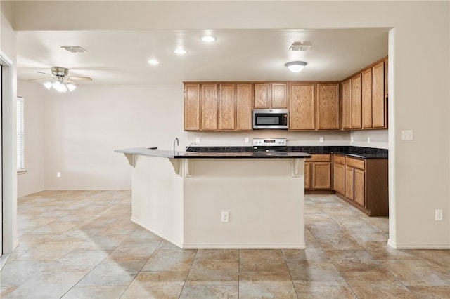 kitchen featuring appliances with stainless steel finishes, an island with sink, sink, a kitchen bar, and ceiling fan