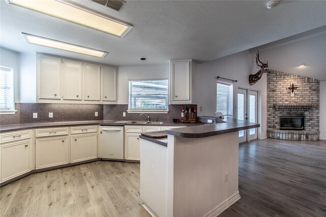 kitchen with a fireplace, white cabinetry, light hardwood / wood-style floors, kitchen peninsula, and lofted ceiling