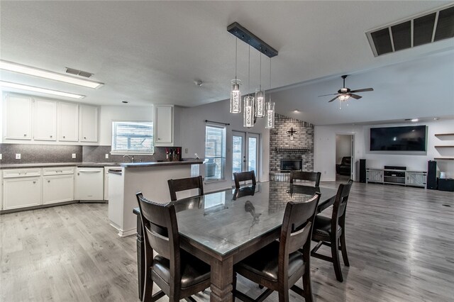 dining space featuring a brick fireplace, vaulted ceiling, sink, ceiling fan, and light hardwood / wood-style flooring