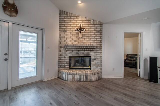 unfurnished living room featuring a brick fireplace, hardwood / wood-style floors, and lofted ceiling