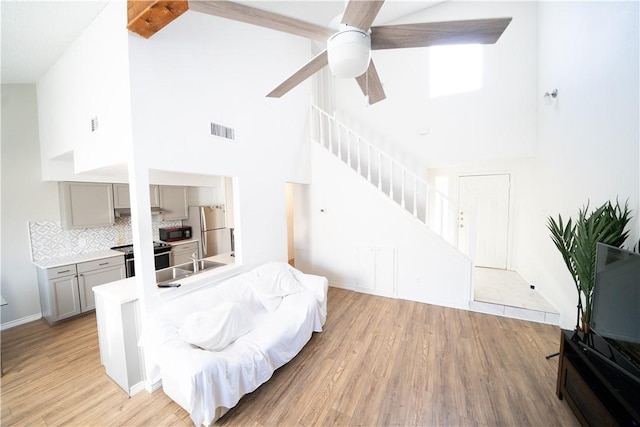 living room with high vaulted ceiling, sink, light hardwood / wood-style flooring, ceiling fan, and beam ceiling