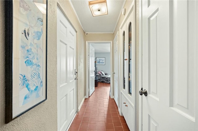 corridor with a textured ceiling, dark tile patterned floors, and ornamental molding