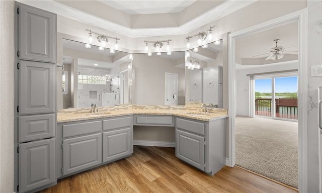 bathroom with a tray ceiling, vanity, wood-type flooring, and ceiling fan