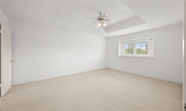 carpeted empty room with ceiling fan and a raised ceiling