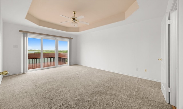 carpeted spare room with a tray ceiling and ceiling fan