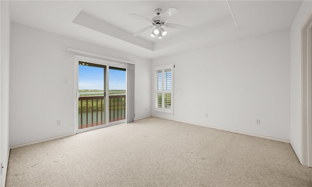 carpeted spare room with a water view, ceiling fan, and a raised ceiling