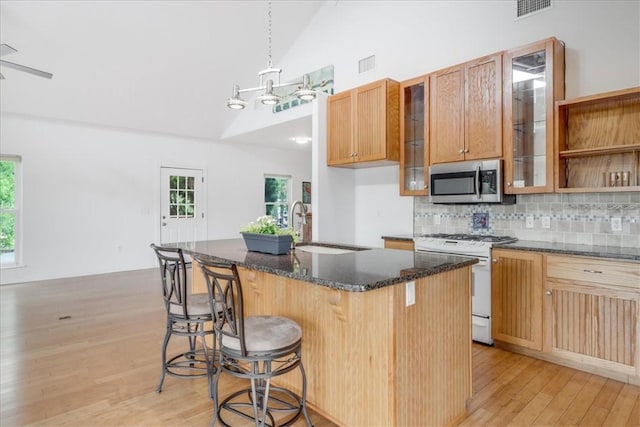 kitchen with a sink, light wood-style flooring, stainless steel microwave, visible vents, and white range with gas cooktop