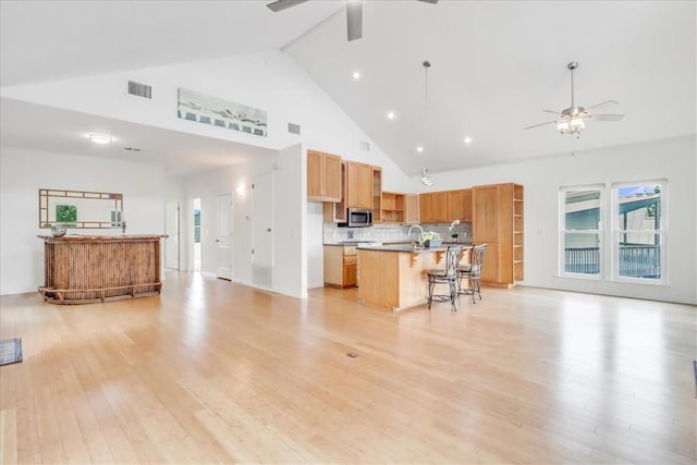 living area with ceiling fan, visible vents, light wood finished floors, and high vaulted ceiling