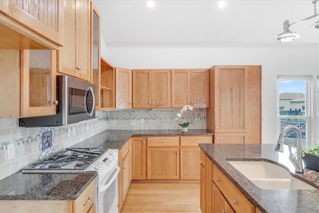 kitchen with white range with gas stovetop, stainless steel microwave, tasteful backsplash, a sink, and light wood finished floors
