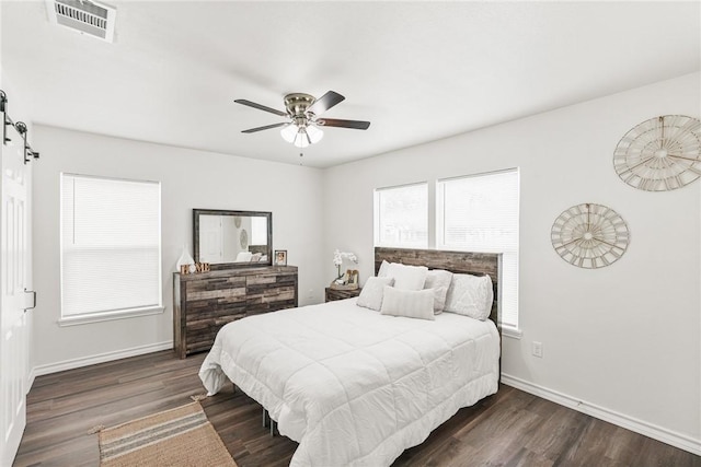 bedroom featuring a barn door, dark wood finished floors, visible vents, and baseboards