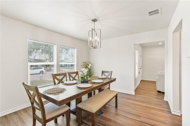 dining room featuring a chandelier, light wood-type flooring, visible vents, and baseboards