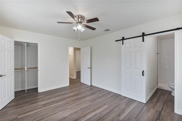 unfurnished bedroom with dark wood finished floors, a closet, visible vents, a barn door, and baseboards