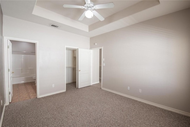 unfurnished bedroom with a raised ceiling, carpet flooring, visible vents, and baseboards