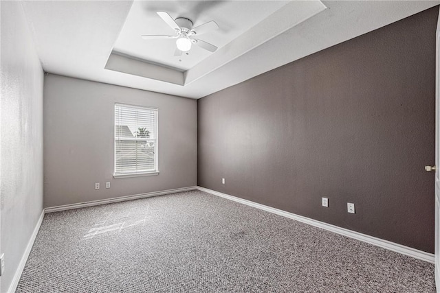 carpeted empty room featuring a raised ceiling, baseboards, and ceiling fan