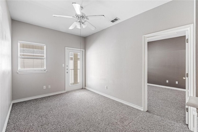 empty room with baseboards, visible vents, carpet floors, and ceiling fan