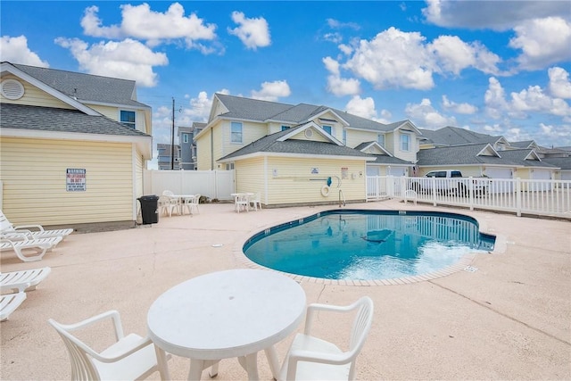 community pool with a patio, fence, and a residential view