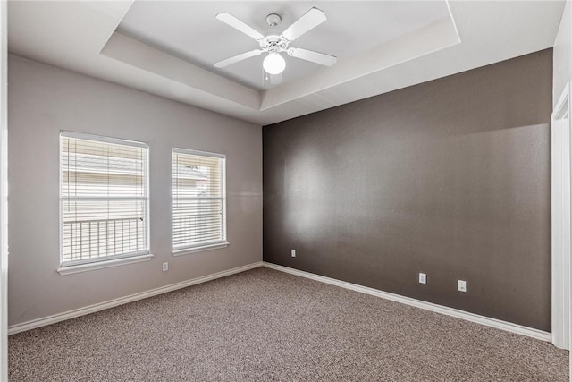 carpeted empty room featuring a raised ceiling, baseboards, and ceiling fan