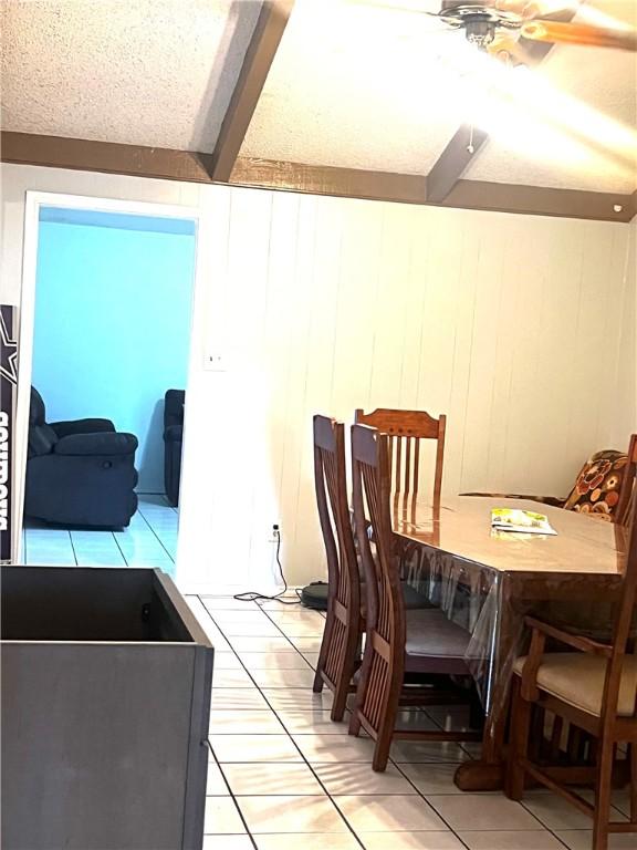 tiled dining area featuring beamed ceiling, ceiling fan, and wood walls