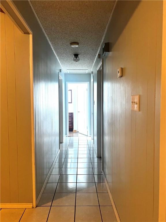 corridor featuring tile patterned flooring, a textured ceiling, crown molding, and wood walls