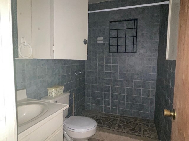 bathroom featuring vanity, toilet, a tile shower, and tile walls